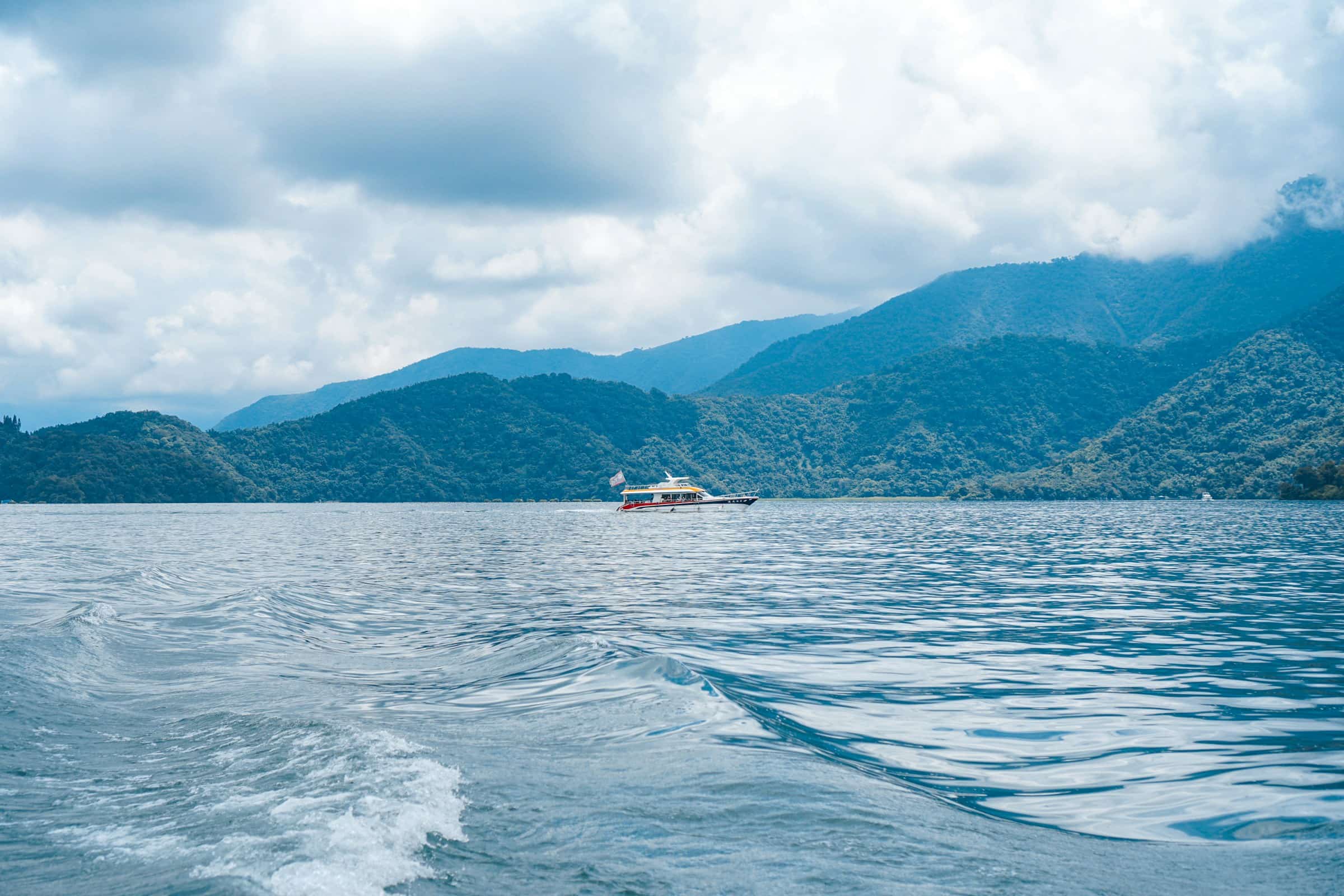 white boat on sea near mountain under white clouds during daytime
